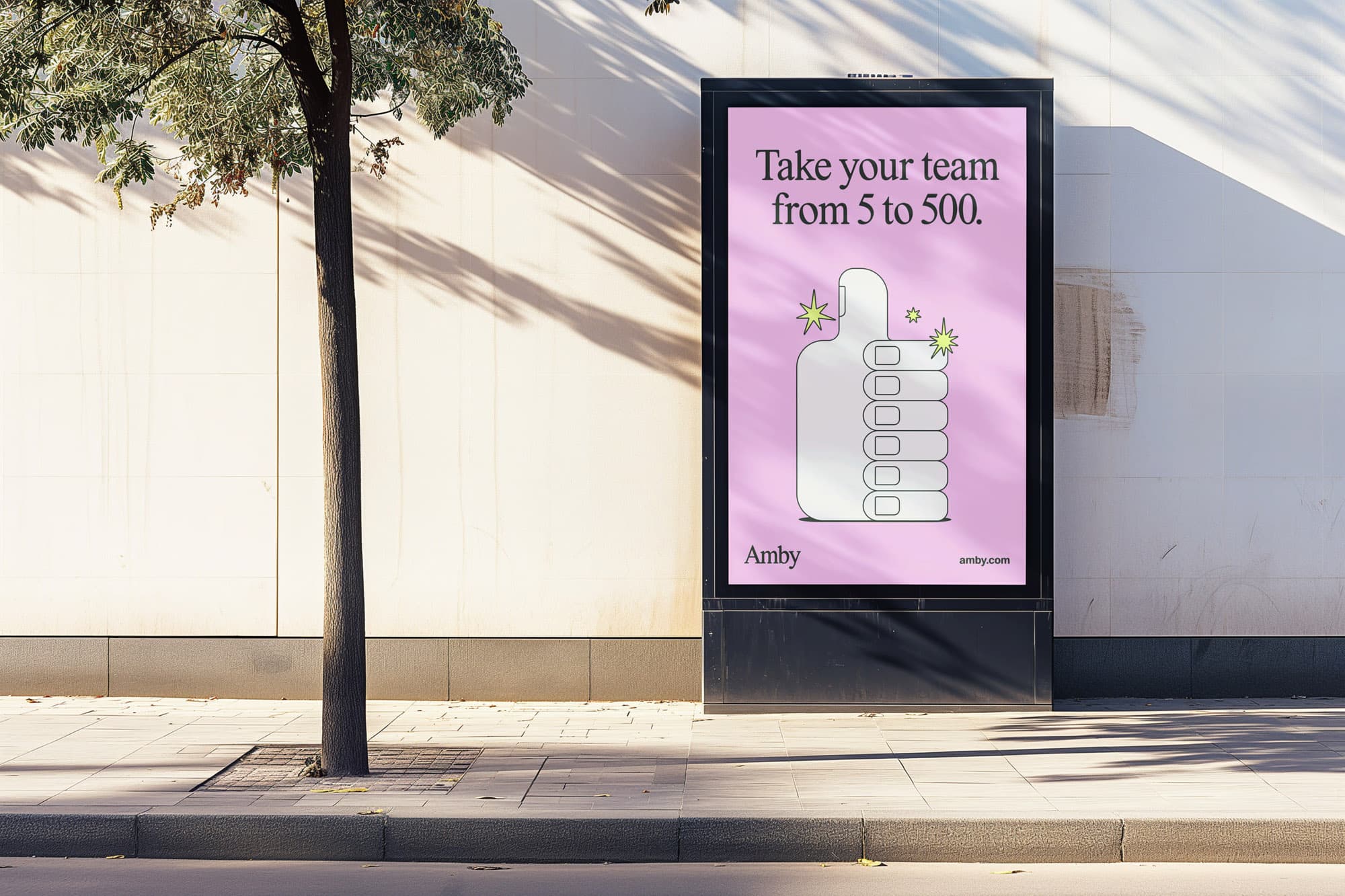 Outdoor citylight ad on a sidewalk beside a tree. The pink poster reads "Take your team from 5 to 500." with an illustrated thumbs-up hand, the Amby logo, and amby.com.