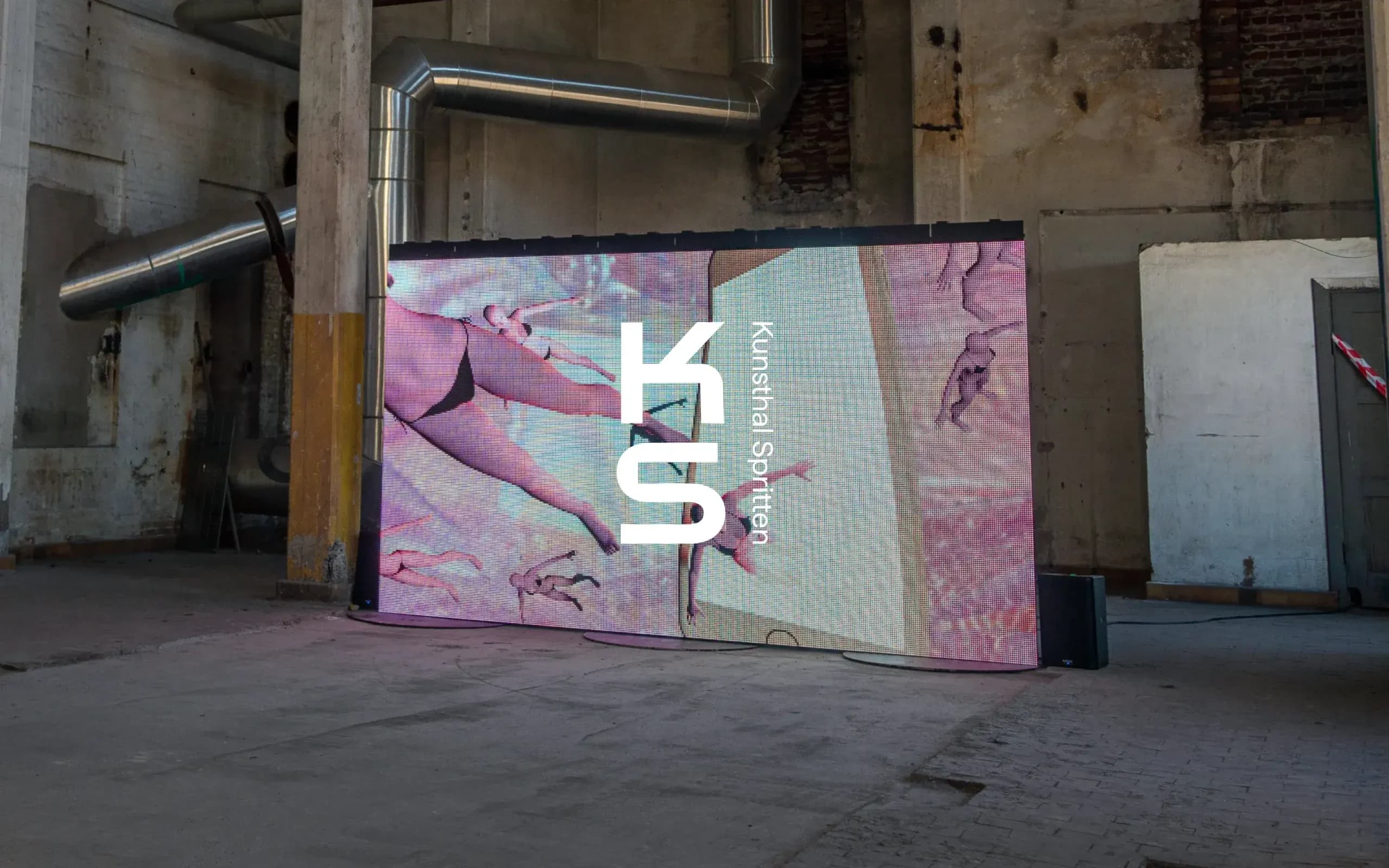 LED screen in a raw industrial building showing the KS logo overlaid on artwork – mockup of digital signage in the Spritten building.